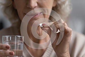 Elderly woman holding pill and glass of water closeup image