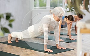 Elderly woman holding plank pose during group yoga training