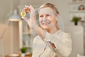 An elderly woman holds a bitcoin coin in her hand and smiles. Senior citizen happy life concept