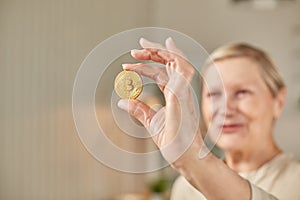 An elderly woman holds a bitcoin coin in her hand and smiles. Senior citizen happy life concept