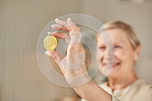 An elderly woman holds a bitcoin coin in her hand and smiles. Senior citizen happy life concept