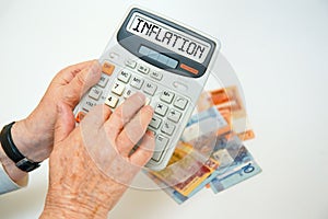 An elderly woman holds a calculator in her hands and calculates expenses. INFLATION inscription on the calculator