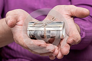 An elderly woman holds in her hands money in a roll, which is tied with a rope. Savings for the period coronavirus and quarantine