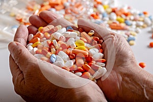 An elderly woman holds a lots of colored pills in hands on a white background.