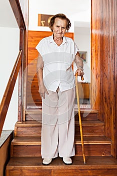 Elderly woman at home using a cane to get down the stairs