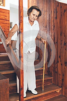 Elderly woman at home using a cane to get down the stairs