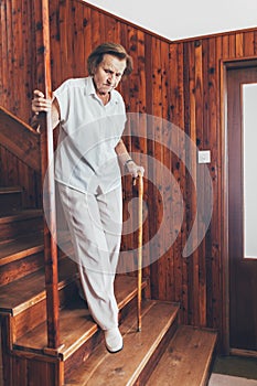 Elderly woman at home using a cane to get down the stairs