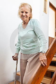 Elderly woman at home using a cane to get down the stairs