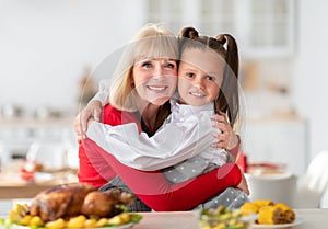 Elderly woman hugging her granddaughter while cooking festive family dinner with yummy turkey at home