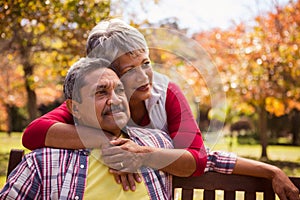 An elderly woman hugs her husband sitting on the bench