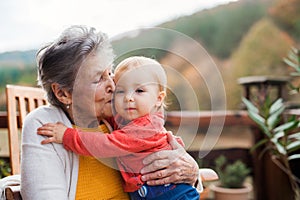 Elderly woman kissing a toddler great-grandchild on a terrace in autumn.
