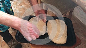An elderly woman kneads bread dough and puts it on a baking sheet. You can see her working hands.