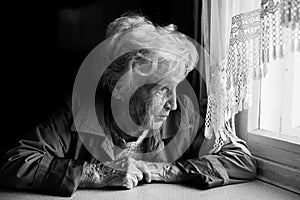 An elderly woman looks longingly out the window. Loneliness. photo