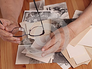 An elderly woman looks at old photographs, recalls her past youth. Hands on the table. Loneliness,, memories photo