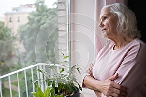 An elderly woman looks sadly out the window.