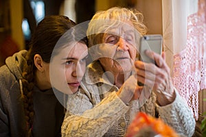 Elderly woman looks at a smartphone, with his adult granddaughter