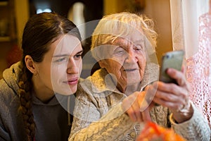 An elderly woman looks at a smartphone his adult granddaughter