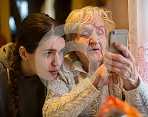 An elderly woman looks at a smartphone, with his adult granddaughter. Family.