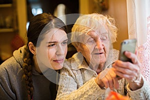 Elderly woman looks and typing on a smartphone, with his adult girl granddaughter. Family.
