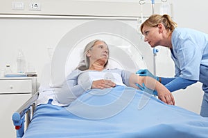 Elderly woman lying in the hospital room bed, nurse disinfect the patient`s arm to injects the vaccine