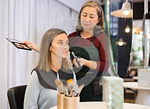 Elderly woman makeup artist working in beauty studio with young female client