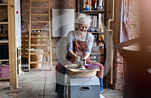 Elderly woman making ceramic work with potter`s wheel