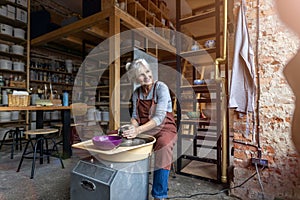 Elderly woman making ceramic work with potter`s wheel