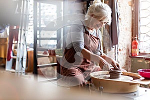 Elderly woman making ceramic work with potter`s wheel