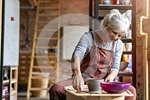 Elderly woman making ceramic work with potter`s wheel