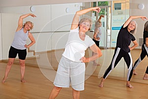 Elderly woman making stretching exercises in fitness studio
