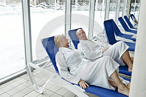 An elderly woman with a man in bathrobes on a sun lounger by the pool