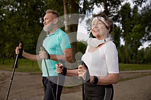 Elderly woman and man married couple enjoying nordic walking in city park