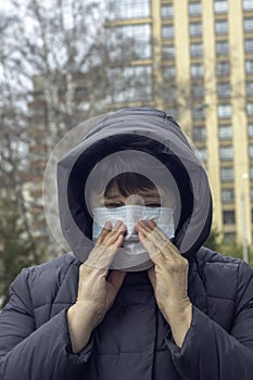 An elderly woman in a medical mask sneezes and coughs, holds her face with her hands photo