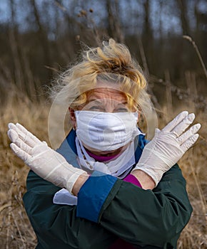 An elderly woman in a medical protective mask and rubber gloves gestures stop coronavirus