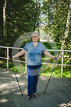 Elderly woman with Nordic walking poles in summer park