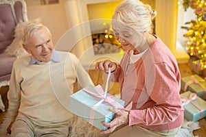 Elderly woman opening christmas gift from her husband and looking anticipated photo