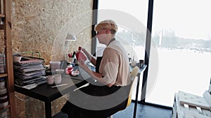 An elderly woman painting ceramic mug with red color