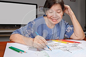 Elderly woman painting color on her drawing at home