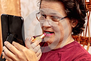 An elderly woman paints her lips with lipstick, taking care of her beauty. Serious elderly woman apply lipstick in front of a