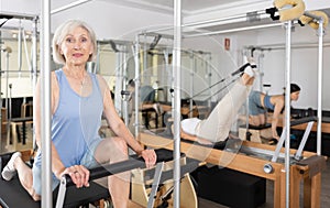 Elderly woman performing set of pilates exercises on reformer