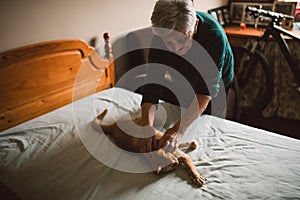 Elderly woman petting her cat on the bed