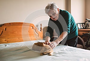 Elderly woman petting her cat on the bed