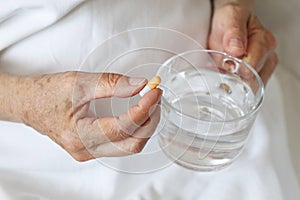 Elderly woman with pill and glass of clean water in wrinkled hands