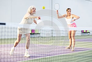 Elderly woman playing pickleball in doubles team with young girl