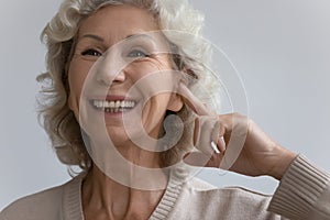 Elderly woman points finger to ear with hearing aid device