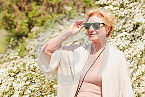 Elderly woman posing among bushes with white flowers