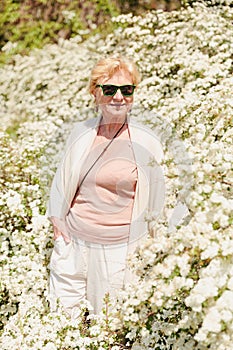 Elderly woman posing among bushes with white flowers