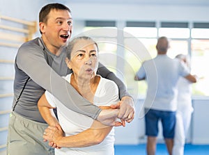 Elderly woman practices strikes and submissions against an attacking man during self-defense lesson in gym