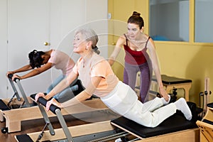 Elderly woman practicing pilates on reformer with young female trainer