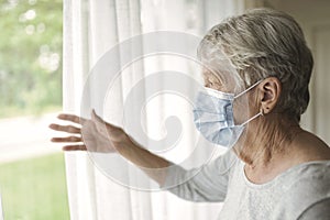 An elderly woman in a protective mask in front of window